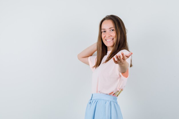 Young woman in t-shirt, skirt inviting to come and looking cheerful , front view.