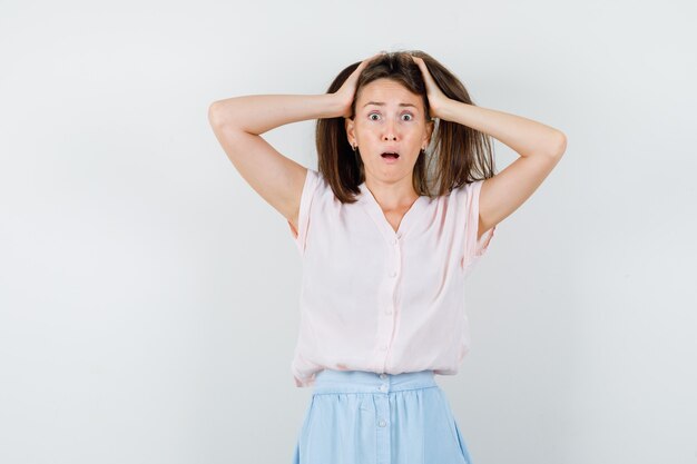 Young woman in t-shirt, skirt keeping hands on head and looking puzzled , front view.