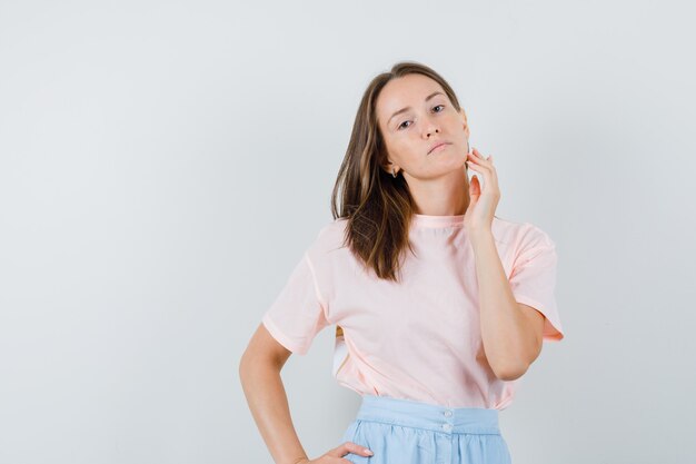 Young woman in t-shirt, skirt posing while looking at camera and looking serious , front view.