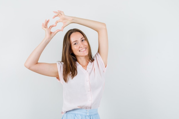 Foto gratuita giovane donna in t-shirt, gonna che mostra il gesto del cuore e che sembra allegra, vista frontale.