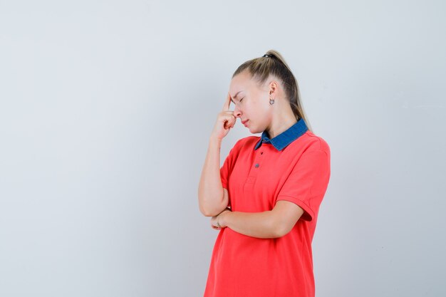 思考ポーズで立っていると疲れているように見えるTシャツの若い女性