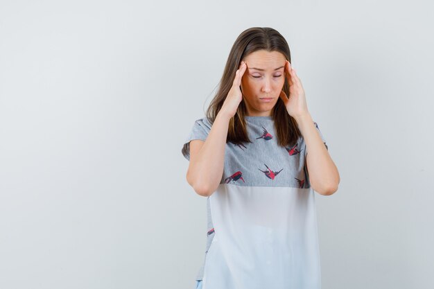 Young woman in t-shirt touching temples with fingers and looking exhausted , front view.