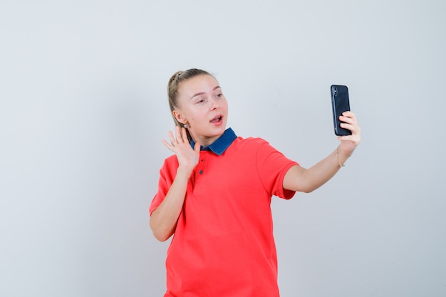 Young woman in t-shirt waving hand on video chat and looking joyful