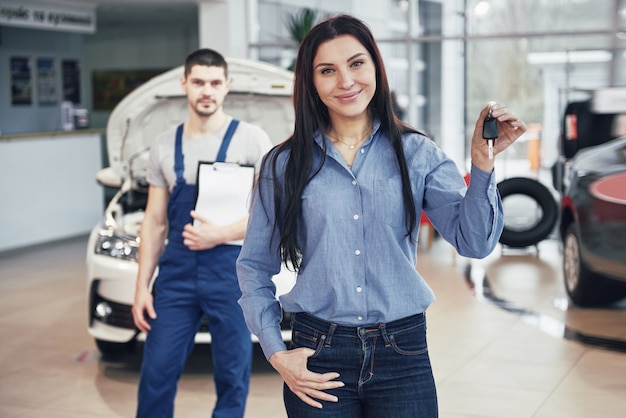 A young woman takes a car from the car service center. She is happy because the work is done perfectly