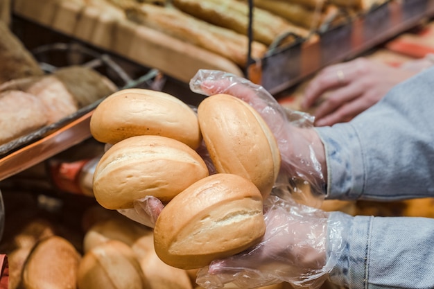 Молодая женщина берет с прилавка в супермаркете свежий хлеб.