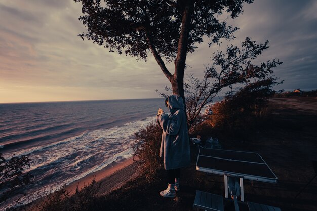 若い女性がスマートフォンで海の夕日の写真を撮る