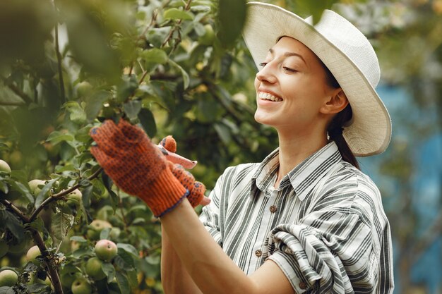 植物の世話をする若い女性。帽子と手袋のブルネット。女性はaveeuncatorを使用します。