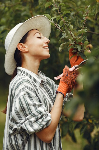 植物の世話をする若い女性。帽子と手袋のブルネット。女性はaveeuncatorを使用します。