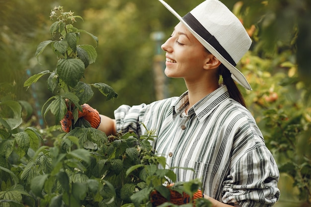 植物の世話をする若い女性。帽子と手袋のブルネット。