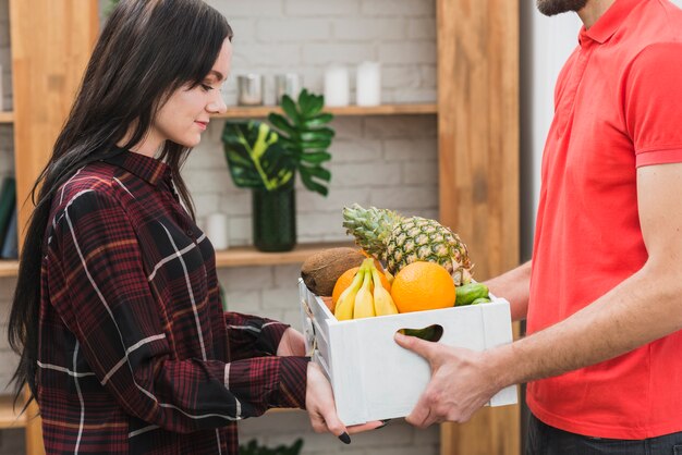 Free photo young woman taking fruit parcel from courier