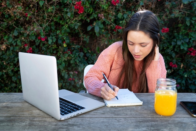 Бесплатное фото Молодая женщина делает заметки на улице, используя ноутбук