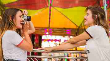 Foto gratuita giovane donna che cattura foto del suo amico sorridente al parco divertimenti