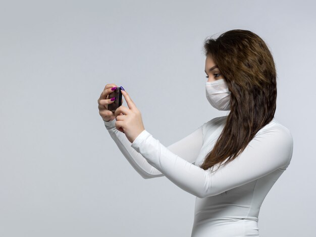 Young woman taking photo of herself in white sterile medical mask