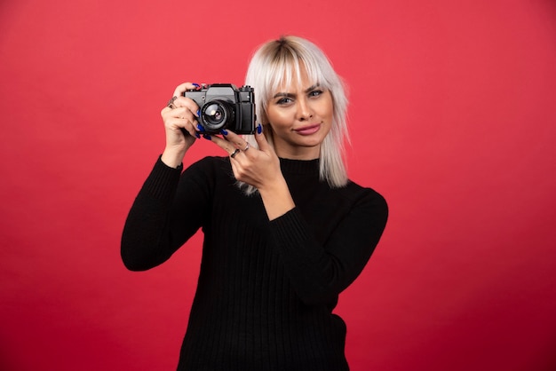 Giovane donna di scattare foto con una fotocamera su uno sfondo rosso. foto di alta qualità