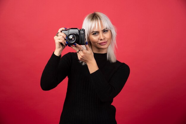 赤い背景の上のカメラで写真を撮る若い女性。高品質の写真