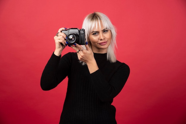 Молодая женщина фотографирует с камерой на красном фоне. Фото высокого качества