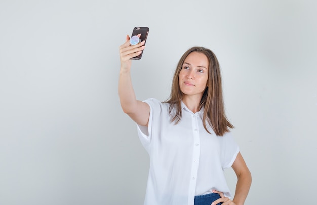 T- 셔츠에 전화에 selfie를 복용하는 젊은 여자