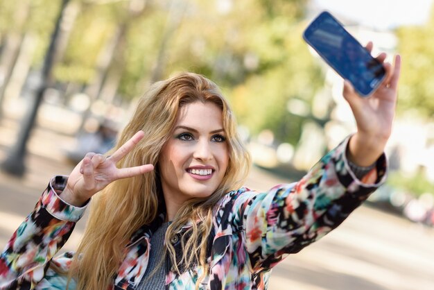 Young woman taking selfie and showing victory gesture