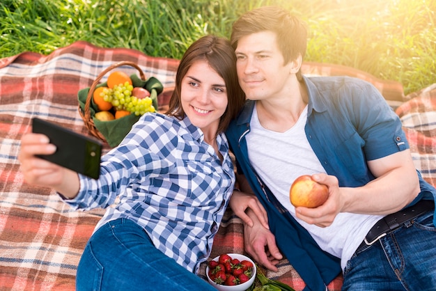 Young woman taking selfie with boyfriend on blanket