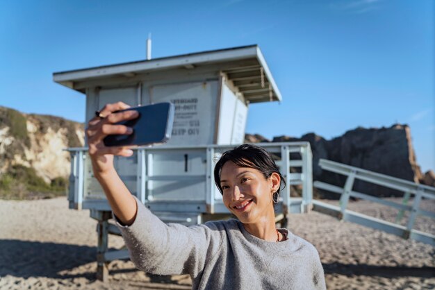 ビーチでスマートフォンで自分撮りをしている若い女性