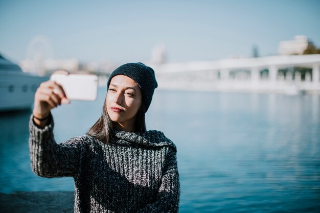 Young woman taking selfie with water in background