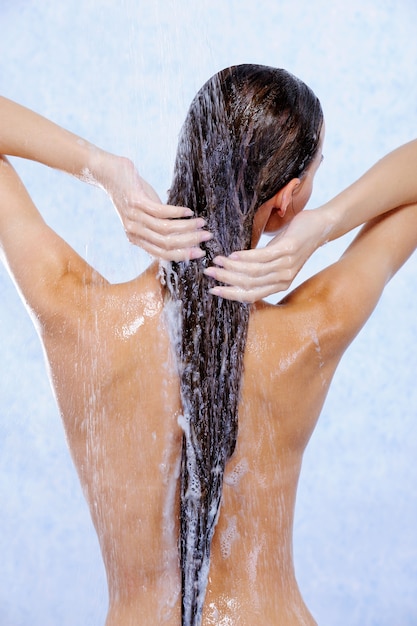 Giovane donna che cattura doccia e si lava i capelli - vista posteriore