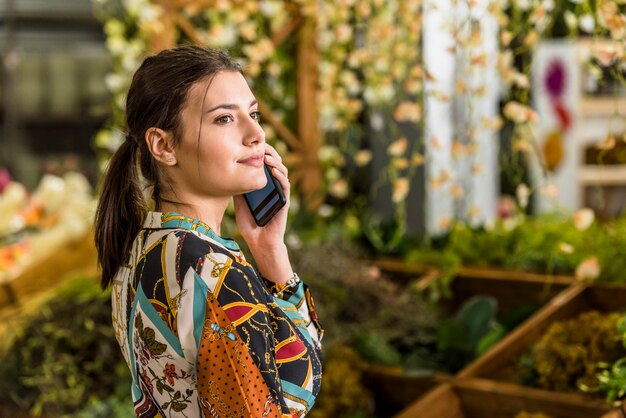 Young woman talking by phone in green house 