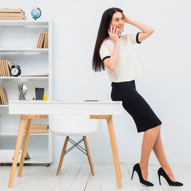 Free photo young woman talking by phone in office