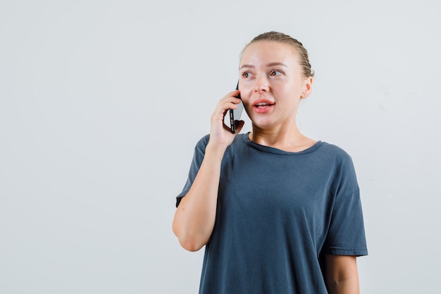 灰色のTシャツで携帯電話で話している若い女性