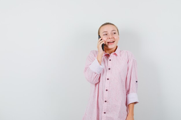 ピンクのシャツを着て携帯電話で話し、陽気に見える若い女性