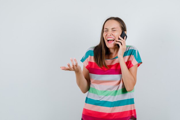 Tシャツを着て携帯電話で話し、幸せそうに見える若い女性、正面図。