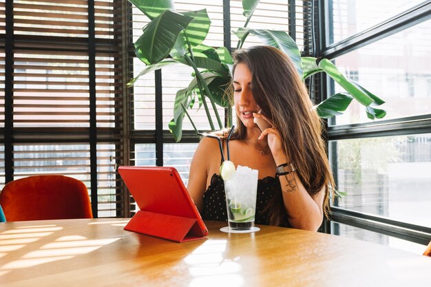 Young woman talking on mobile phone using digital tablet with cocktail glass on table