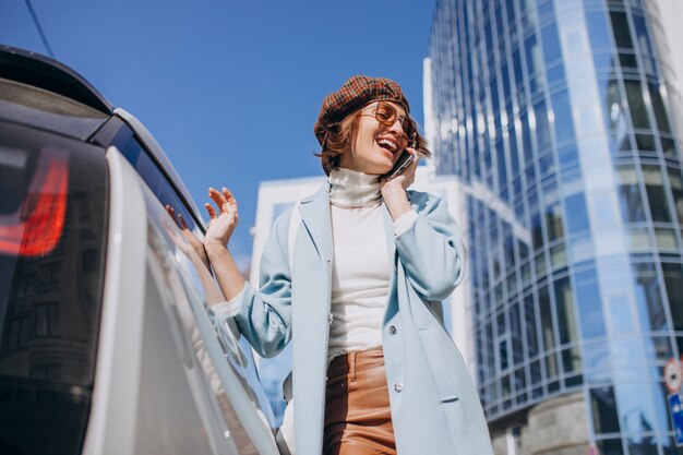 Young woman talking on the phone by electro car in the center