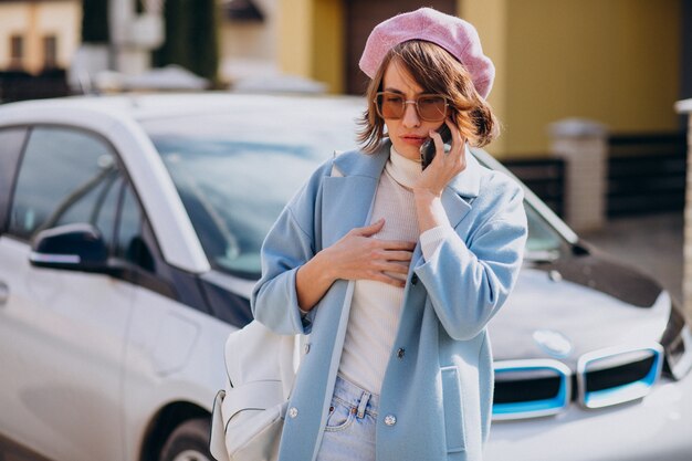 Young woman talking on the phone by her electric car