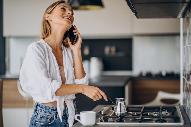 電話で話し、朝のコーヒーを作る若い女性