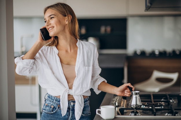 Young woman talking on the phone and making morning coffee