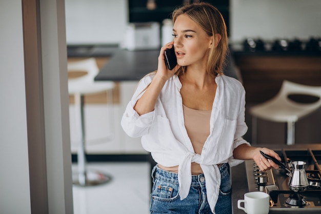 Young woman talking on the phone and making morning coffee