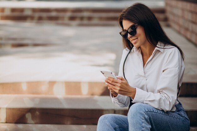 電話で話し、階段に座っている若い女性