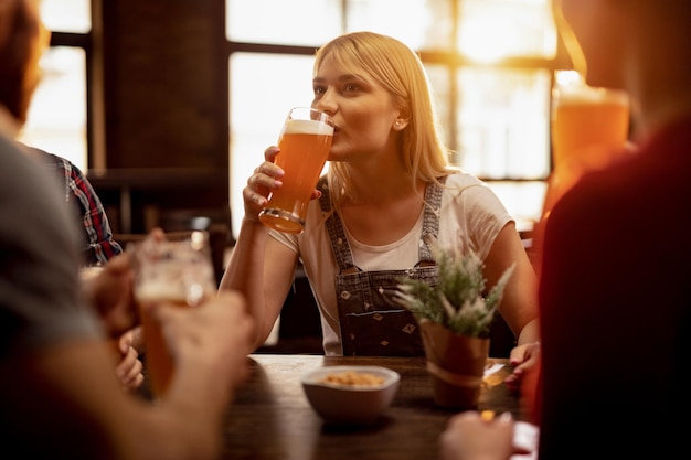 Young woman tasting lager beer while relaxing with friends in a bar