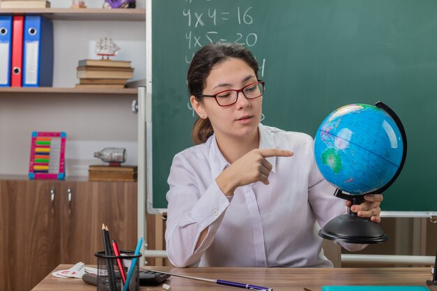 수업을 설명하는 지구본을 들고 안경을 쓰고 젊은 여자 선생님