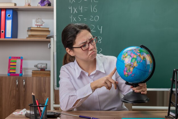 Young woman teacher wearing glasses holding globe