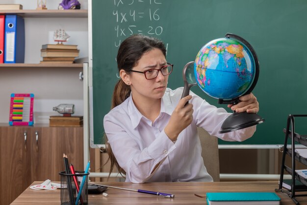 Young woman teacher wearing glasses holding globe