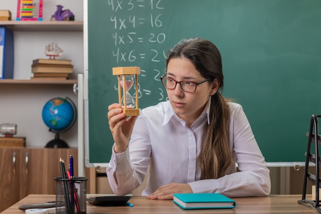 Young woman teacher wearing glasses with hourglass looking at it
