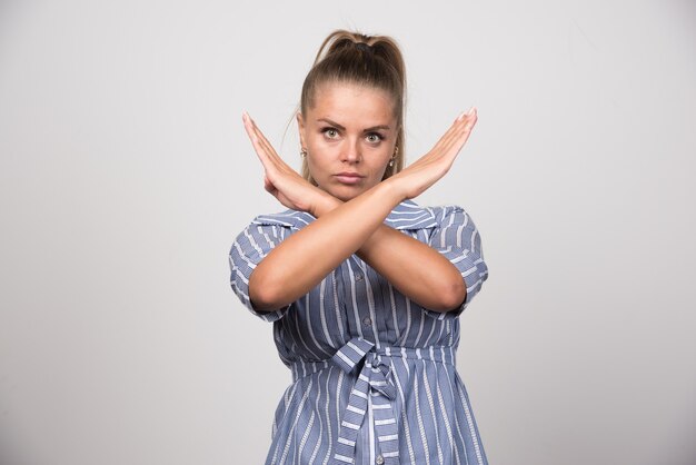 Young woman telling stop on gray wall.