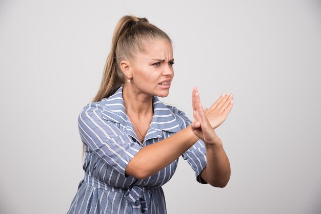 Young woman telling stop on gray wall.