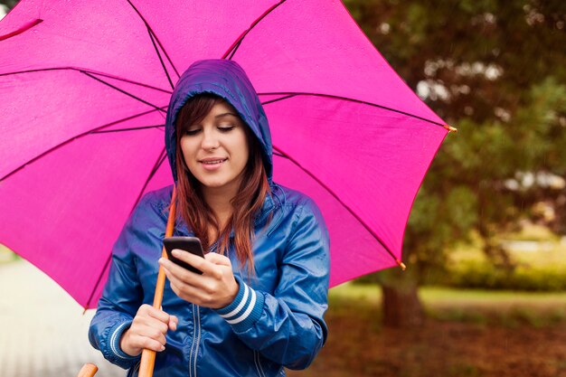 雨の中で携帯電話で若い女性のテキストメッセージ