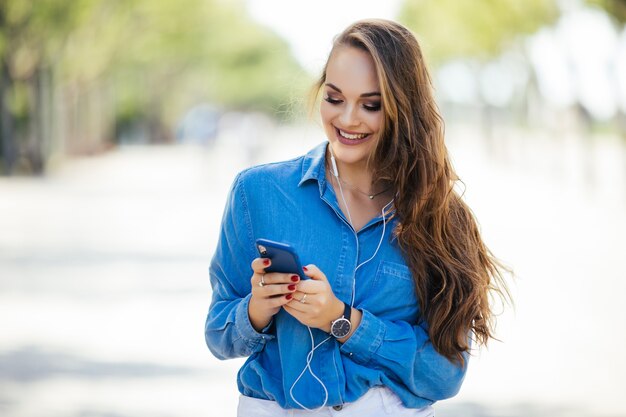 晴れた日に通りを歩いているスマートフォンで若い女性のテキストメッセージ