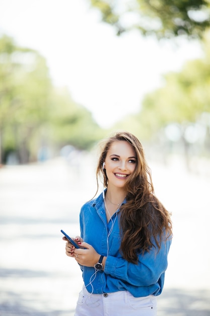 Giovane donna che manda un sms sul telefono astuto che cammina per strada in una giornata di sole