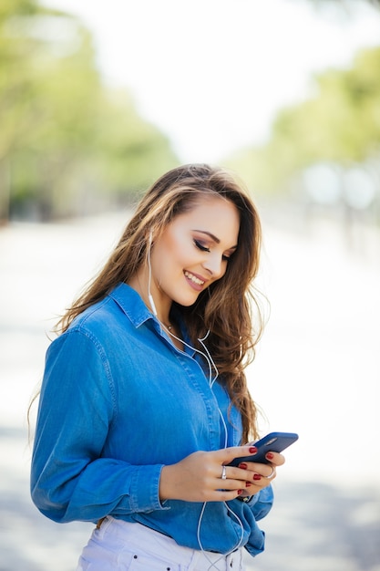 晴れた日に通りを歩いているスマートフォンで若い女性のテキストメッセージ