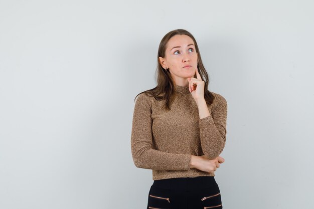 Young woman thinking in golden blouse and looking pensive , front view. space for text